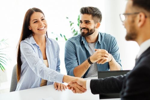A man and a woman shake hands with their real estate agent at their kitchen table