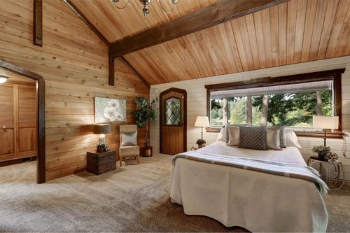 Wooden bedroom interior with high beamed ceiling, grey carpet floor and large bed with neatly arranged pillows