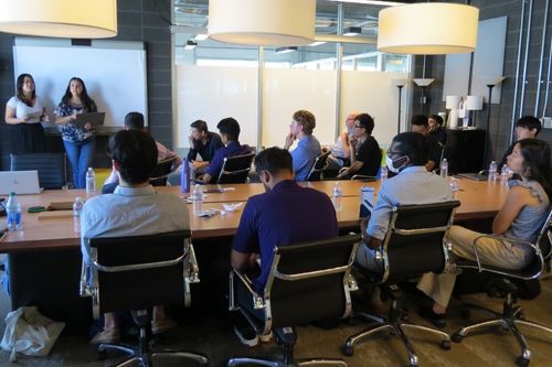 The 2022 class of Windermere-UW College of Built Environment Aspire interns in a conference at Windermere Real Estate headquarters. Three interns are giving a presentation while the rest watch from the conference table.