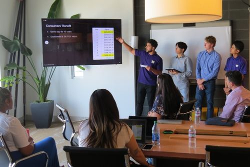 The 2022 class of Windermere-UW College of Built Environment Aspire interns in a conference at Windermere Real Estate headquarters. Four interns are giving a presentation while the rest watch from the conference table.