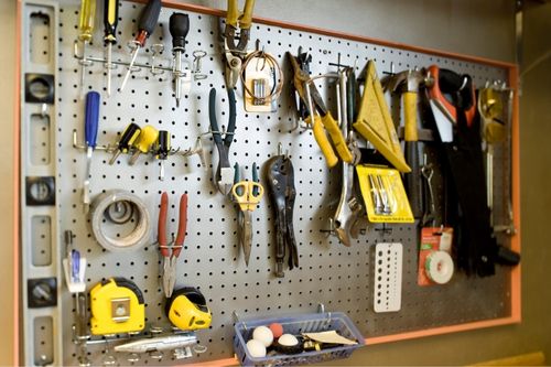 A hardboard hanging panel in a garage full of common hand tools like screwdrivers, measuring tape, scissors, duct tape, vice grips, etc.