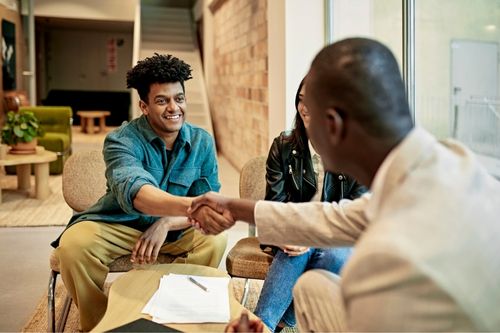 In a modern office, a man and woman shake hands with their real estate agent as they go over the terms of a real estate contract.