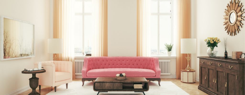 A living room with art deco decorations including long sheer golden curtains, a regal tufted pink couch, gold wall art, and a dark wooden coffee table and dresser.