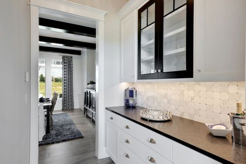 A look through a modern kitchen to a butler’s pantry with a separate entrance. The shelves are stocked with silverware and china.