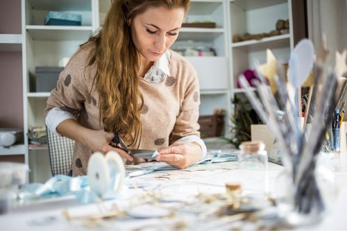 A woman cuts shapes out of construction paper in her craft room.