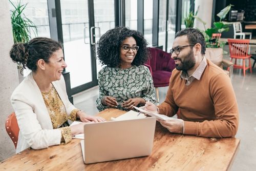 A man and woman homeowner couple discuss the terms of a mortgage buydown program with their mortgage broker in a modern office setting.