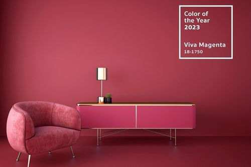 A section living room of a living room with an art deco-style side table and a rounded fabric chair. The wall, chair, and table are all magenta. On the wall, there’s a graphic showing Pantone’s Color of the Year 2023 Viva Magenta and its Pantone color code: 18-1750.