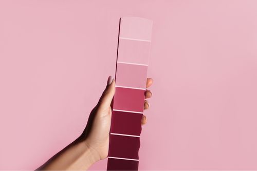 A hand holds up a paint swatch of a magenta color palette containing Pantone’s Color of the Year 2023: Viva Magenta.
