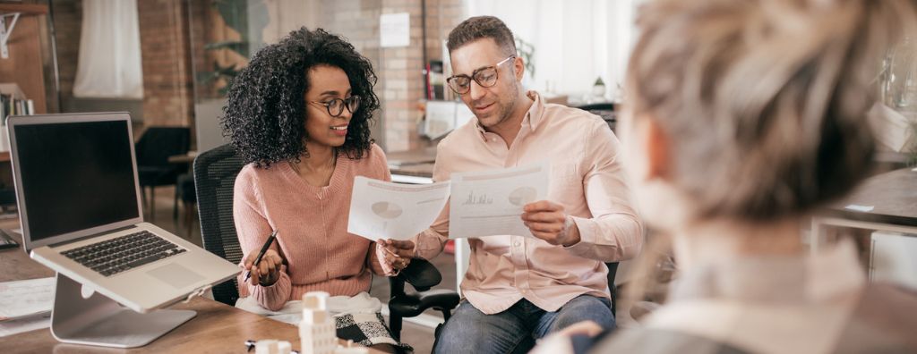 A man and woman homeowner couple review financial paperwork with their mortgage broker in a modern office.