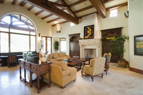 The interior of a brown and white English Tudor style house with exposed wood ceiling beams. The furniture is soft Victorian-style, and the accent pieces are dark mahogany wood.