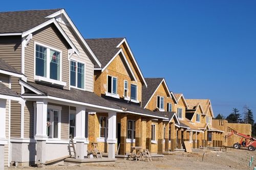 A row of tract new construction homes in a newly developed suburban neighborhood. The home in the foreground is finished, the rest in the row are framed but without siding.