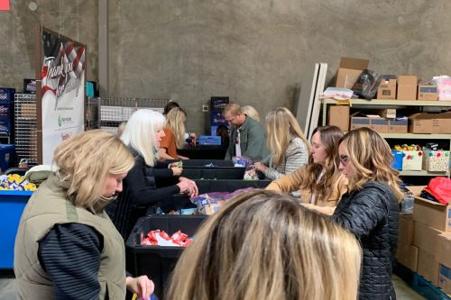 A group of agents and staff from Windermere Utah volunteering in a warehouse. They are putting together donation kits for a local organization Granite Education.