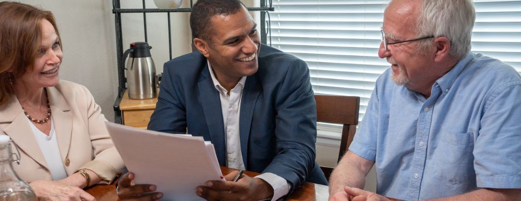 An older heterosexual Caucasian couple talks to an important person during their home buying process, their real estate agent. The real estate agent smiles as they review the terms of a real estate contract.