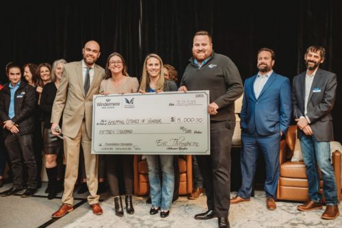 A group of agents and staff from Windermere Northern Colorado presenting a check for $15,000 to the organization Stepping Stones of Windsor onstage at a forecast event.