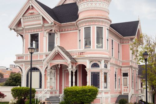 A street-level view of a pink Victorian architecture home with rounded windows, decorative trim, and ornate crown molding.