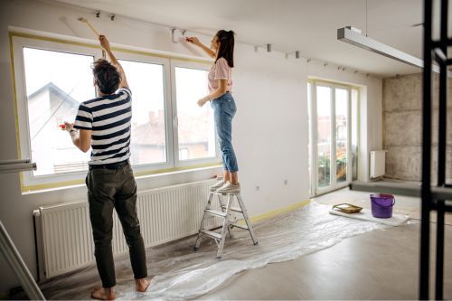 As an example of turnkey vs. fixer-upper homes, a heterosexual Caucasian couple are remodeling their fixer-upper property. They are re-painting the interior to prepare the property for renters.