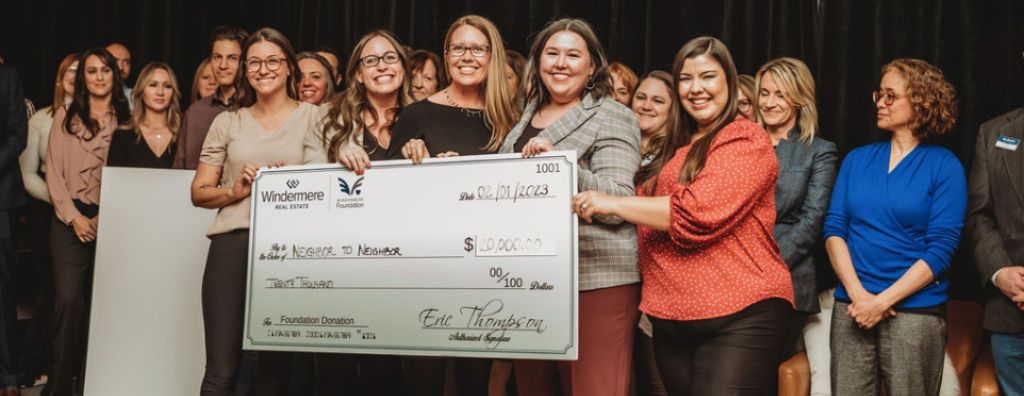 A group of agents and staff from Windermere Fort Collins presenting a check for $20,000 to the organization Neighbor to Neighbor onstage at an event.