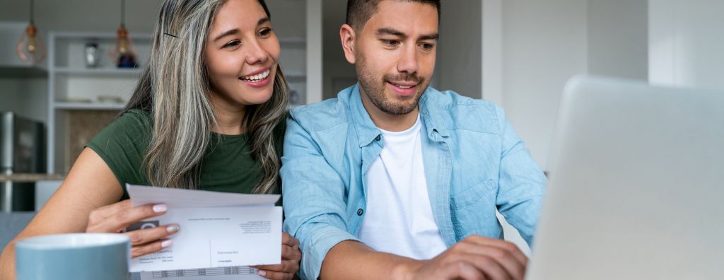 A happy heterosexual Latin American couple on their laptop figuring out how to pay for a house.