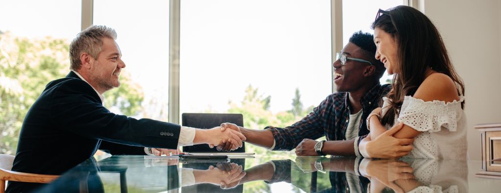 A real estate agent shows his clients how to negotiate as a seller. The clients are a heterosexual couple: a Black man and Asian woman.