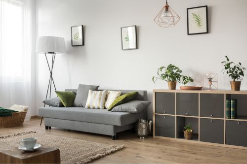 A living room with minimal decorations that show how to design a small space, with elements of multifunctional design throughout the open living room including a multi-purpose couch and a convertible shelving unit.