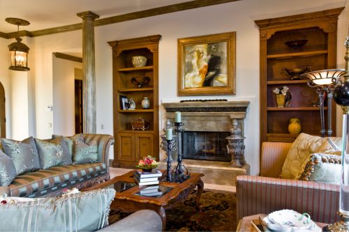 An example of traditional interior design: a classic living room with dark wood built in shelves, metal light fixtures, decorative candle holders, and a patterned carpet over hardwood flooring.