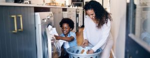 A Black mother and her son are pulling laundry from the washing machine as they work together to keep a tidy home.