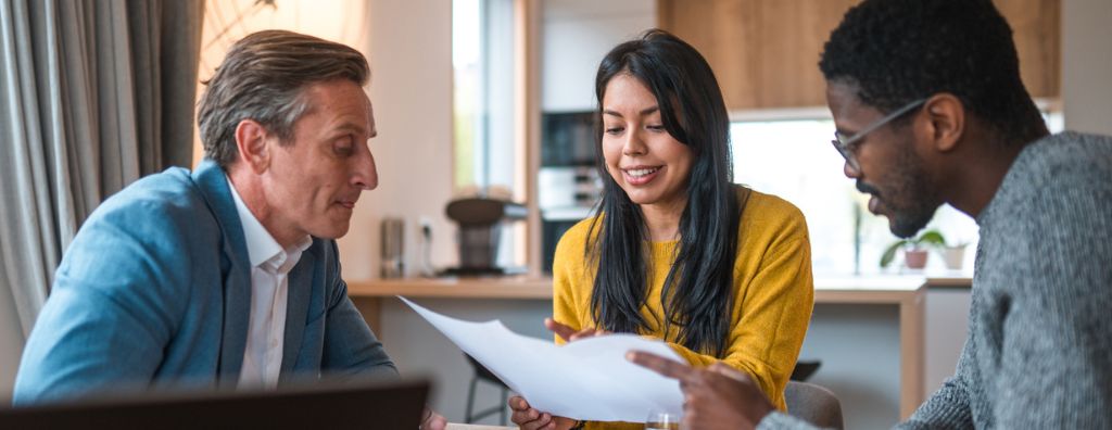 A White real estate agent explains fair market value to an interracial heterosexual couple (Asian woman and Black man) selling their home.