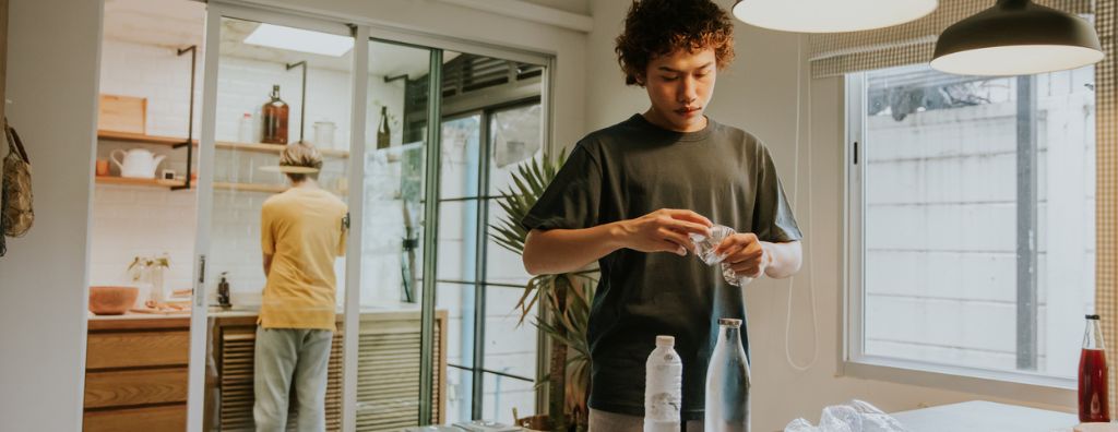 A young man is finding ways to save and reuse water at home. He recycles water bottles and uses others to store water.