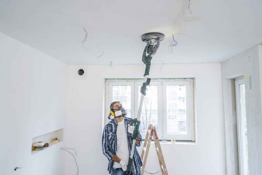 
Man using vacuum sanding machine on ceiling and walls