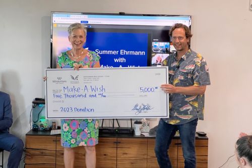 A man and a woman hold up a check for $5,000 from the Windermere Utah office, presented to the Make-A-Wish Foundation.