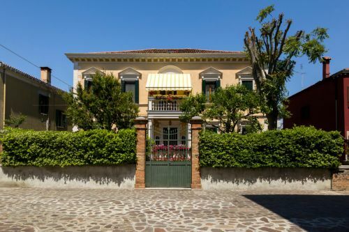 An example of Italianate architecture: a stucco two-story house with dressed windows, a central awning on the top floor, and a gated entry. The house’s exterior is a classic Tuscan yellow.