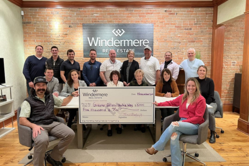 A large group of people pose smiling in the Windermere Bozeman, MT office with a giant check made out to Greater Gallatin United Way for $5,000.