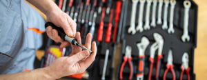 Hands hold a tool above a blurred out toolbox.