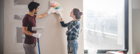 A young man and woman look at paint swatches against a wall of their home as they remodel.